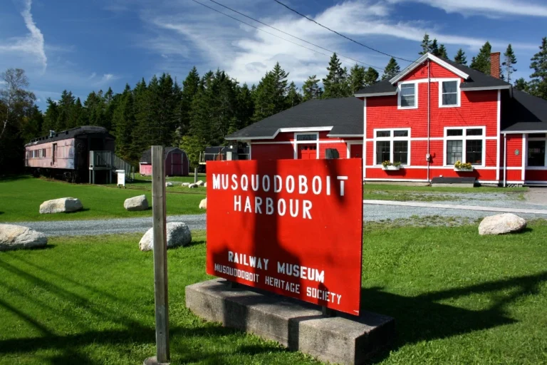 Red Musquodoboit Harbour Railway Museum sign in front of the restored red railway station and a vintage passenger car